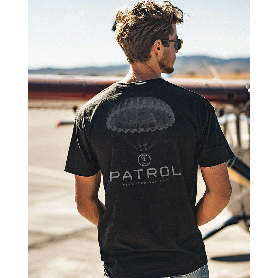 A man wearing the Patrol parachute blueprint tee, stood on a runway, outdoors, 100% cotton unisex tee